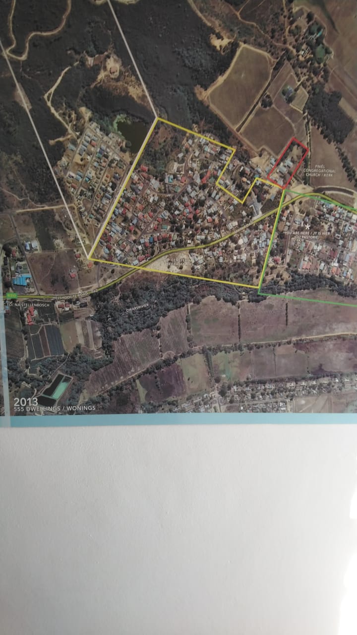 An aerial photograph display of Pniël village with coloured boundary lines and the caption 2013 · 555 dwellings / wonings.