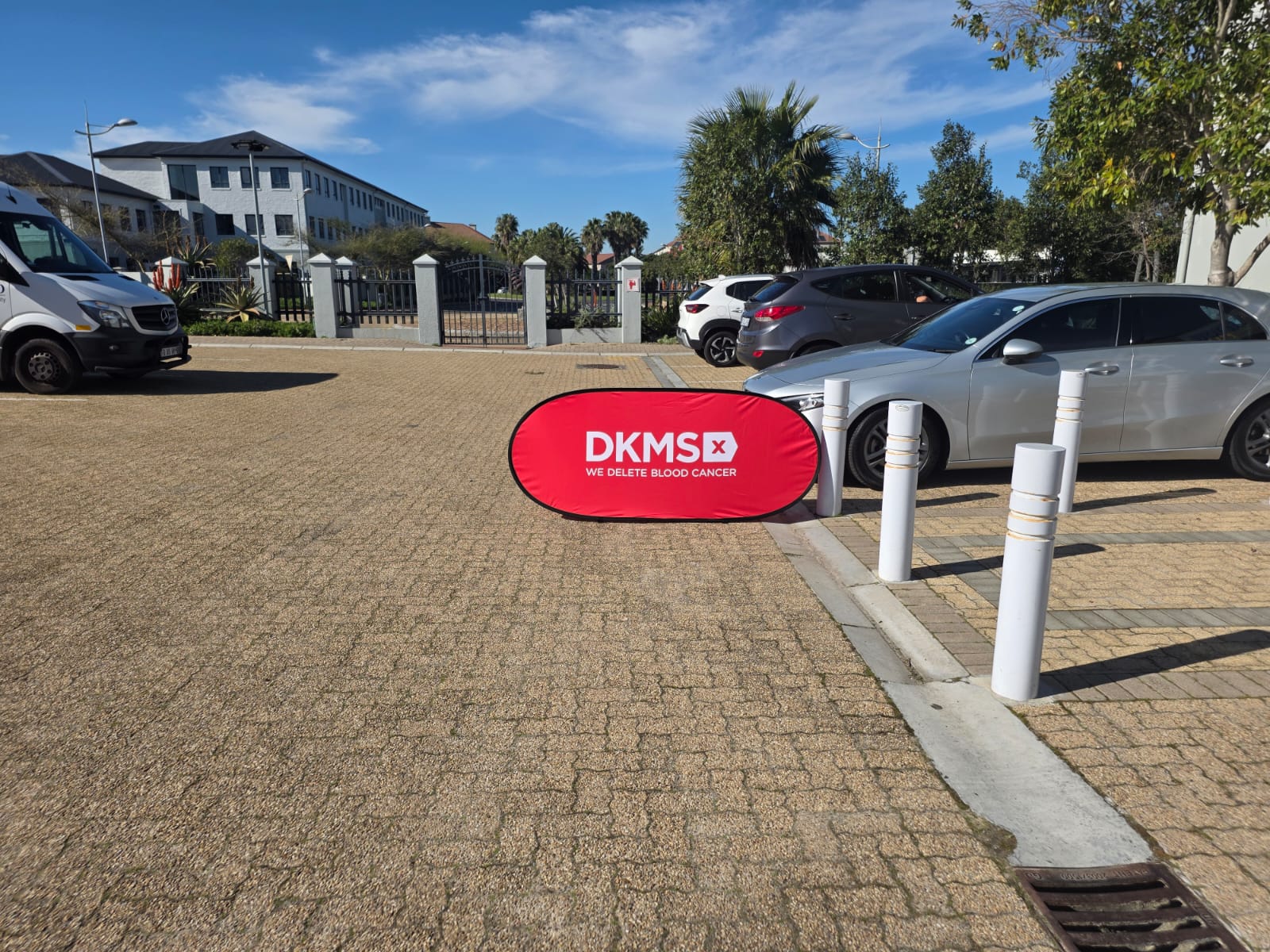 A DKMS Africa banner standing outside the venue in morning sunlight.