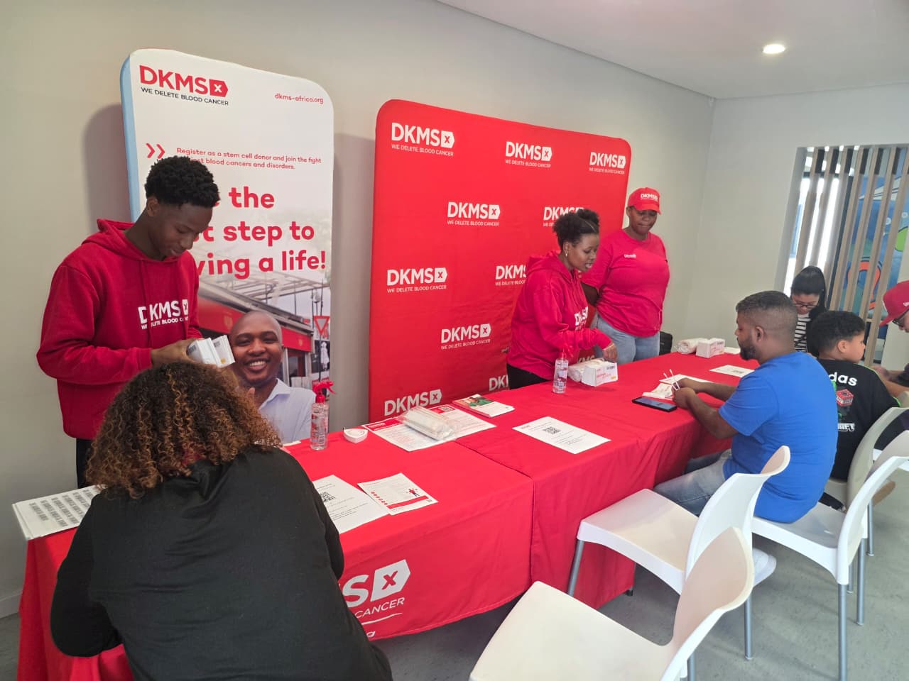 DKMS Africa volunteers in red assisting visitors with registration at a long red table.