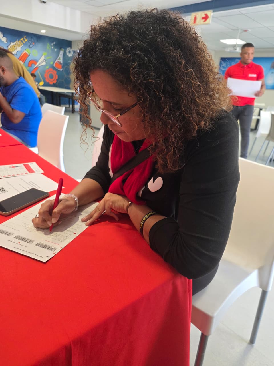 A woman completing a stem cell donor registration form at a red-draped table.